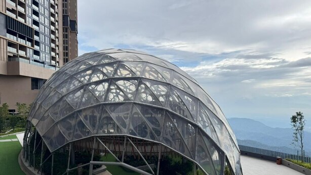 Une structure moderne en forme de dôme, dotée d’un design géométrique, entourée d’un espace paysager agrémenté d’un sentier et de verdure.