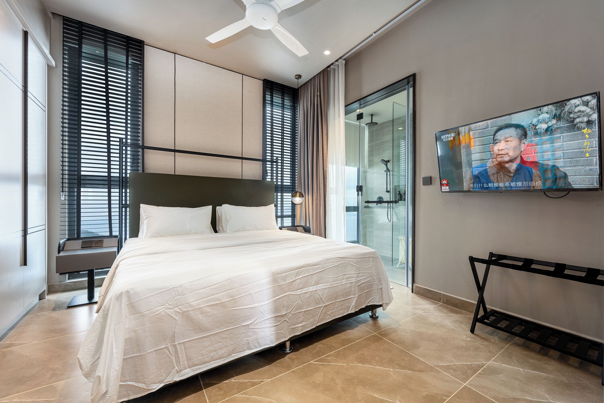 A modern hotel room with a large bed, a TV mounted on the wall, and a bench by the window.