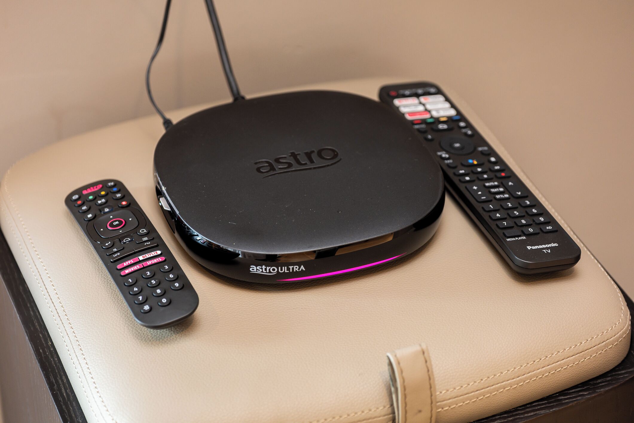 A black Astro ULTRA router on a beige leather chair with two remote controls beside it.