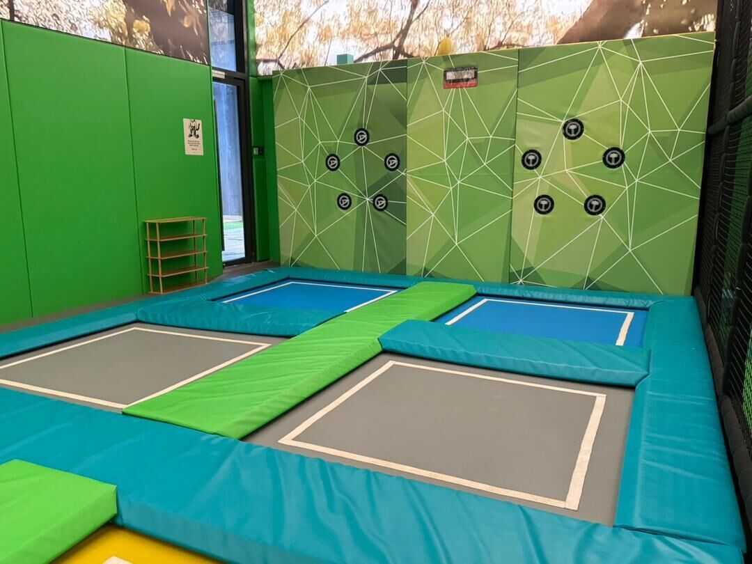 An indoor trampoline area with two trampolines and safety padding.