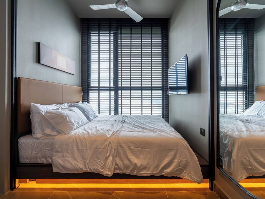 Un dormitori modern amb un llit gran, un ventilador de sostre i una finestra amb persianes.
