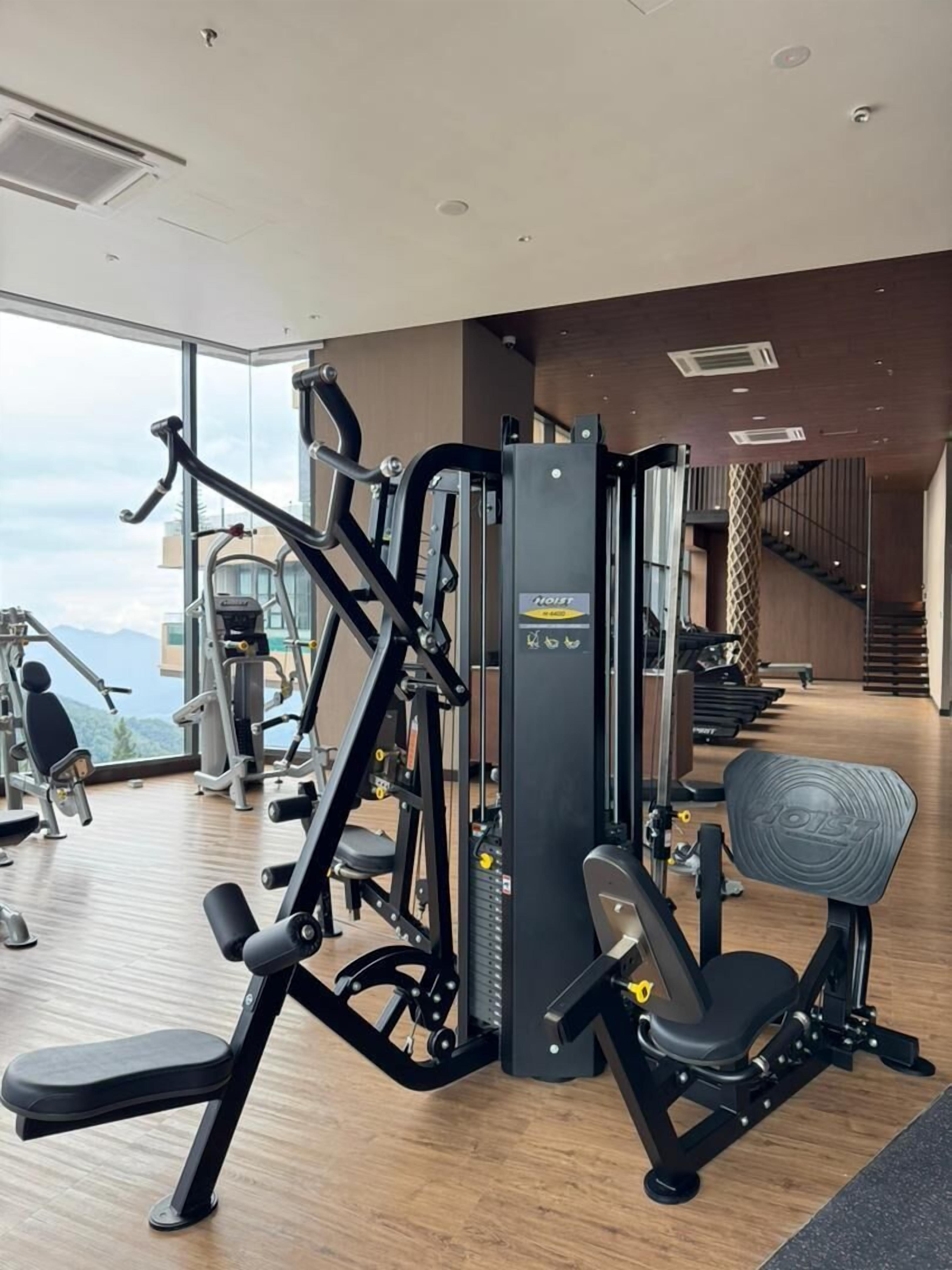Une salle de sport moderne équipée de divers appareils d’exercice, avec un escalier et une vue sur la ville.