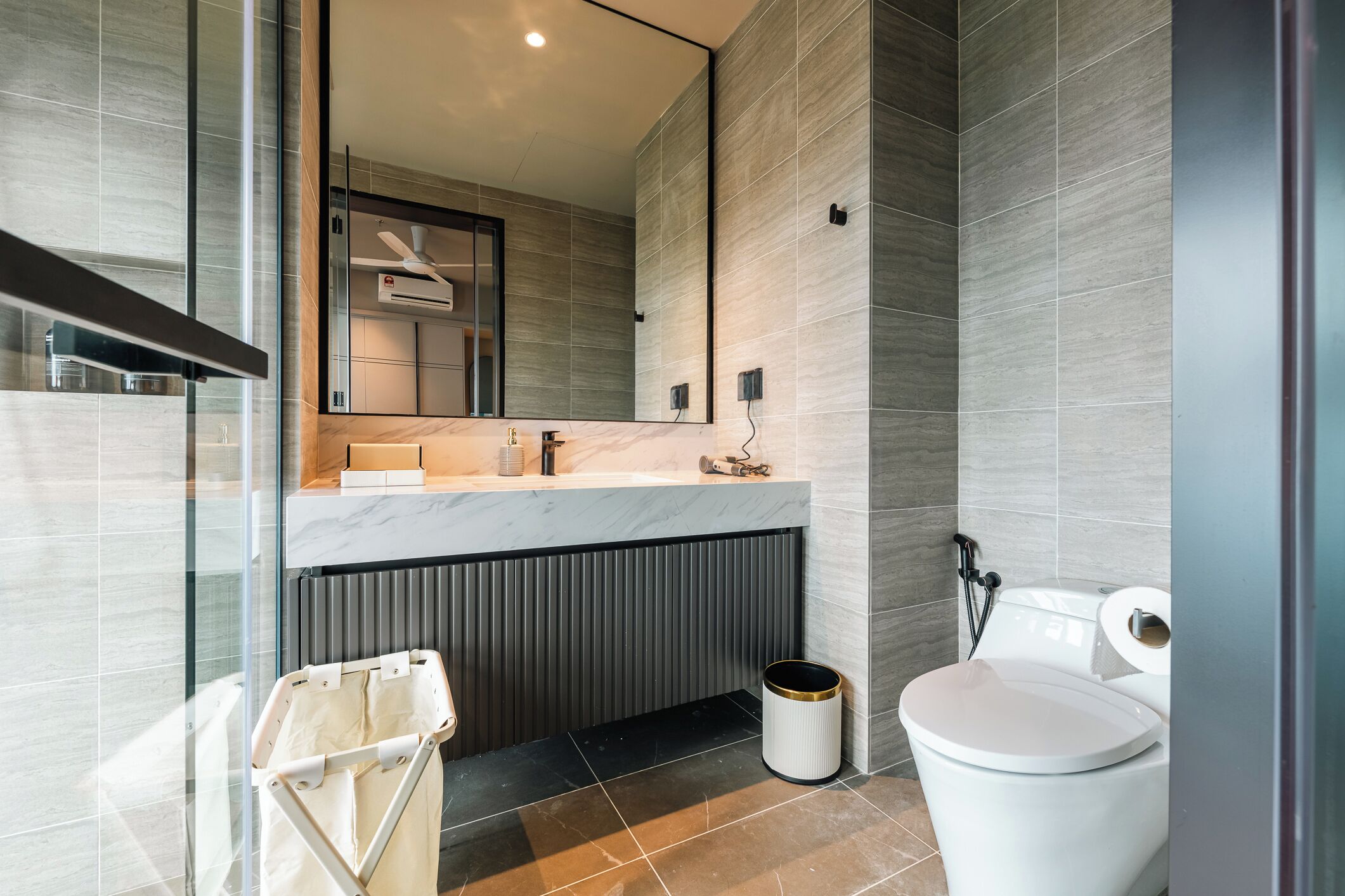 Un baño moderno con encimera de mármol, inodoro y cubo de basura.