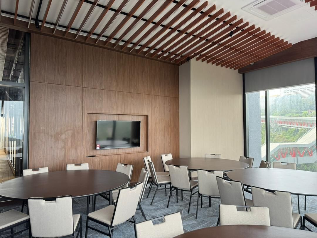 A modern conference room with a large table and chairs, a mounted TV, and large windows offering a view of the city.
