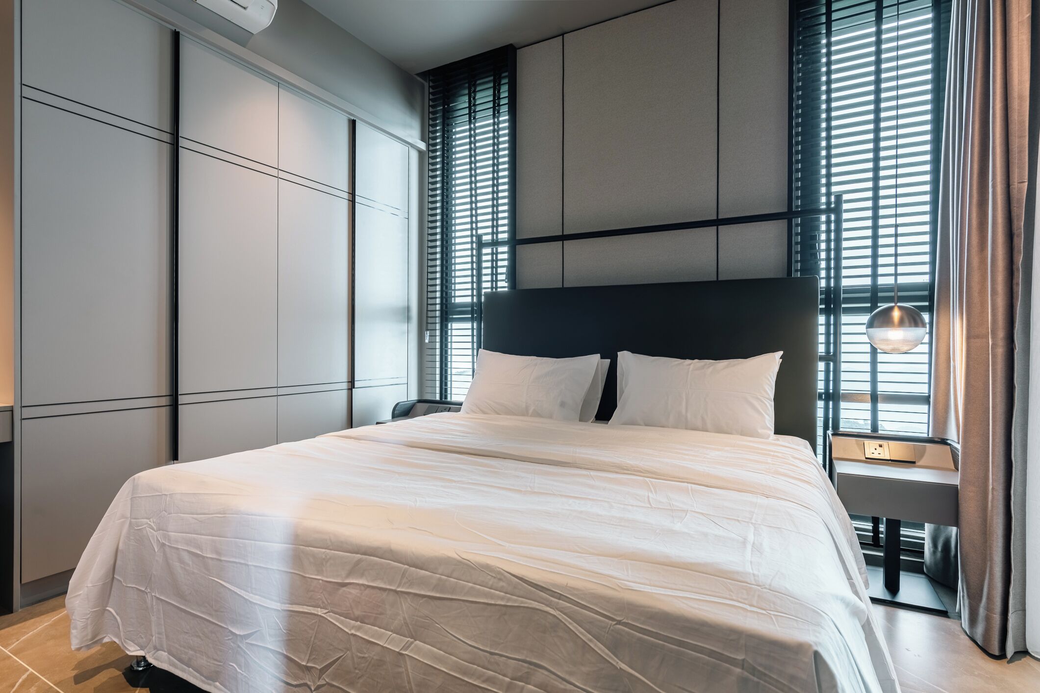 A modern hotel room with a large bed, built-in wardrobe, and a bedside table with a lamp.
