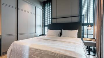 A modern hotel room with a large bed, built-in wardrobe, and a bedside table with a lamp.