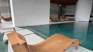 Un espace aménagé au bord de la piscine, avec un fauteuil de relaxation en bois et une piscine.