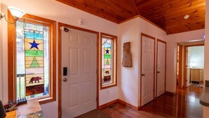 Um corredor com pisos de madeira e portas brancas, que leva a um quarto com teto de madeira.