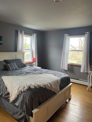 Une chambre à coucher avec un lit, une table de chevet, une fenêtre avec des rideaux et une vue sur l’extérieur.