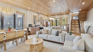 Un'ampia zona giorno con soffitto in legno, un divano grande, un tavolo da pranzo con sedie e una cucina sullo sfondo.