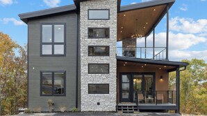 Una moderna casa a due piani con facciata in pietra, ampie finestre e un patio in legno.