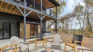 Un patio extérieur moderne, doté de fauteuils Adirondack, d’un foyer et d’un bâtiment avec une terrasse en bois et de grandes fenêtres.