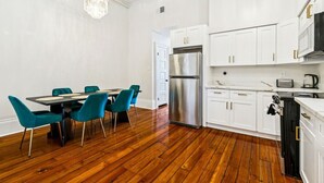 Une cuisine moderne avec des meubles blancs, un réfrigérateur en acier inoxydable et un coin repas doté de chaises de couleur turquoise.