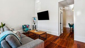 Un salon comprenant un canapé, une table basse, un téléviseur fixé au mur et une bibliothèque.