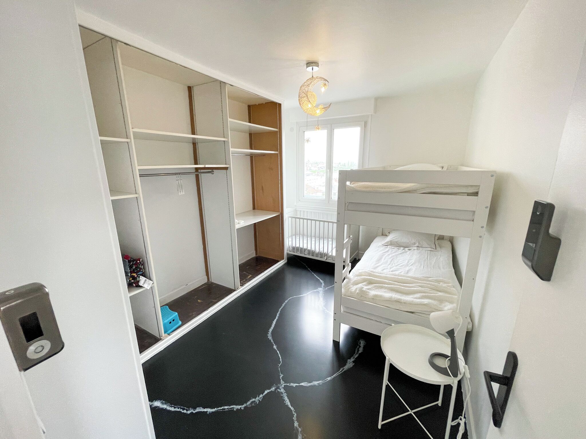 A bunk bed with a small table and chair, a wardrobe with multiple shelves, and a ceiling light fixture.
