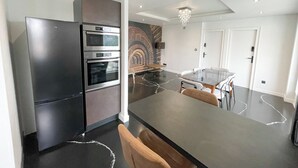Une cuisine moderne dotée d’un four encastré, d’un coin repas avec une table en verre et d’un mur décoratif en briques.