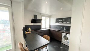 Une cuisine moderne avec un plan de travail noir, un lave-linge encastré et une grande fenêtre.
