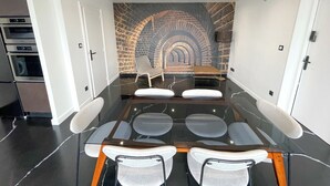 Une salle de réunion moderne avec une table en verre, des chaises blanches, une fresque murale en briques et un lustre.