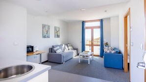 En moderne lejlighed med tekøkken, en grå sofa, en blå lænestol og spiseplads.