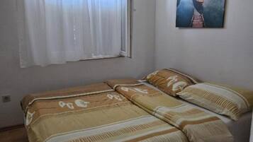 Une petite chambre avec un lit simple, une fenêtre ornée de rideaux blancs et un tableau accroché au mur.