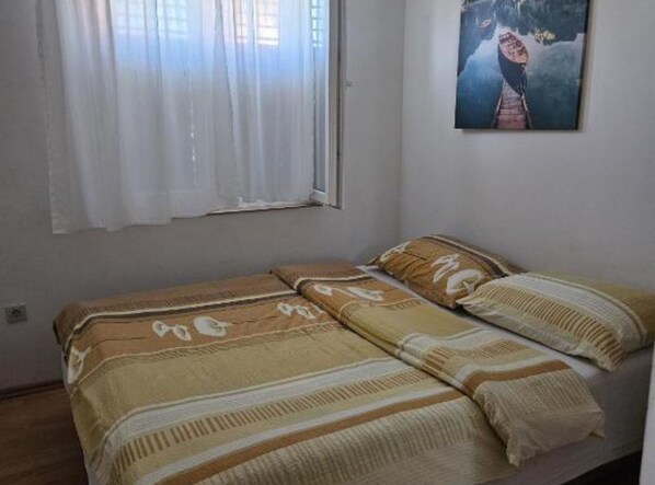 A small bedroom with a single bed, a window with white curtains, and a painting on the wall. - Holiday Home Green Oasis Lika (Lovinac)