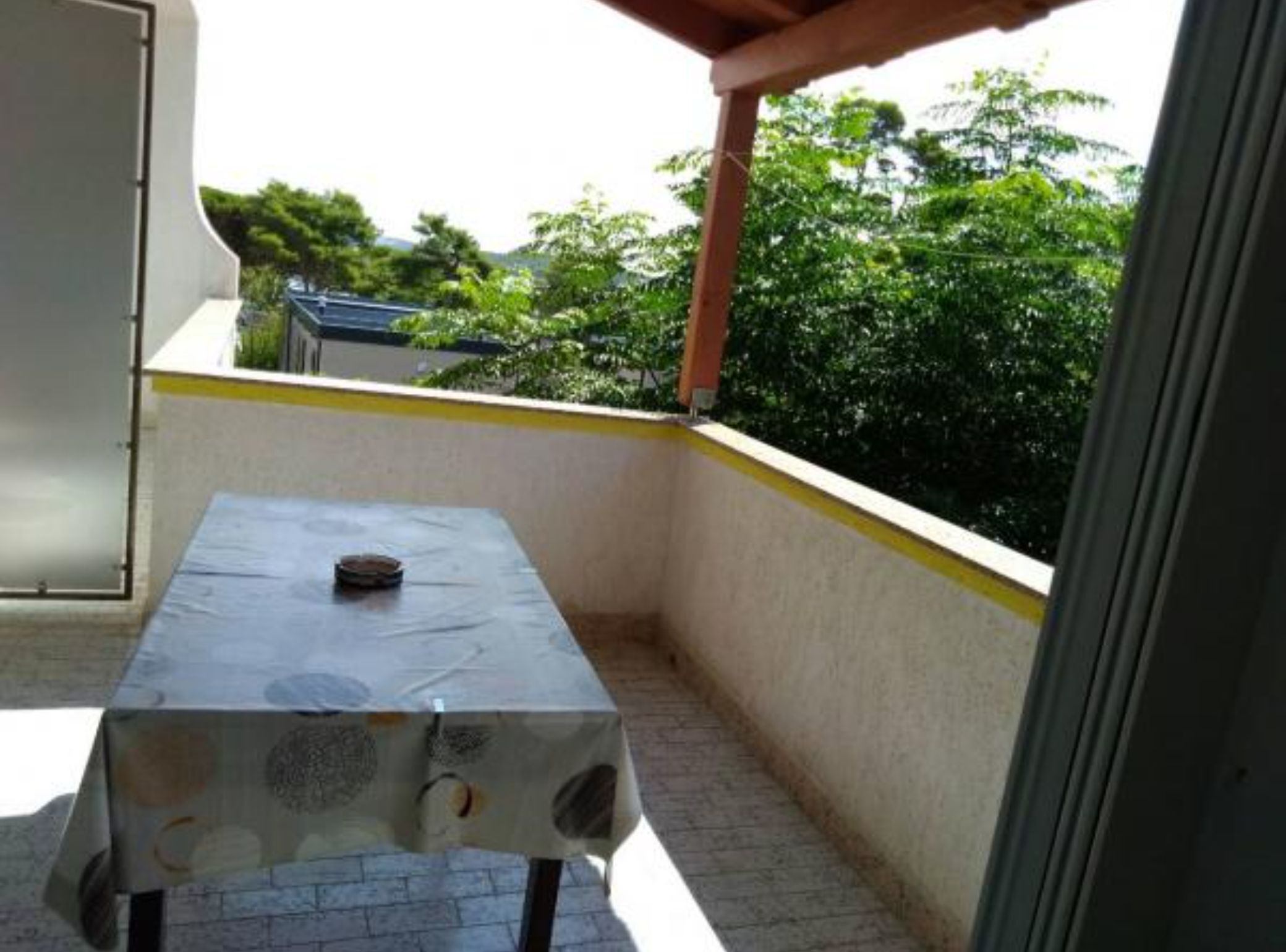 Een klein balkon met een tafel en stoelen, uitzicht op groen en een gebouw op de achtergrond.