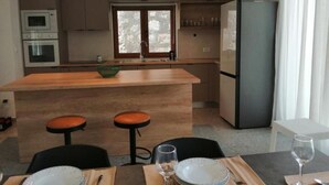 A modern kitchen with a central island, bar stools, a refrigerator, and a dining table set for two. - House Serenity (Vrgorac)