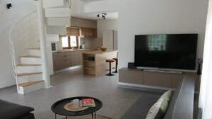 A modern living room with a sofa, a coffee table, and a TV. There is a staircase leading to an upper floor. - House Serenity (Vrgorac)