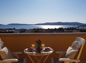 En balkon med et bord dækket til morgenmad, med udsigt over vand og fjerne bakker.