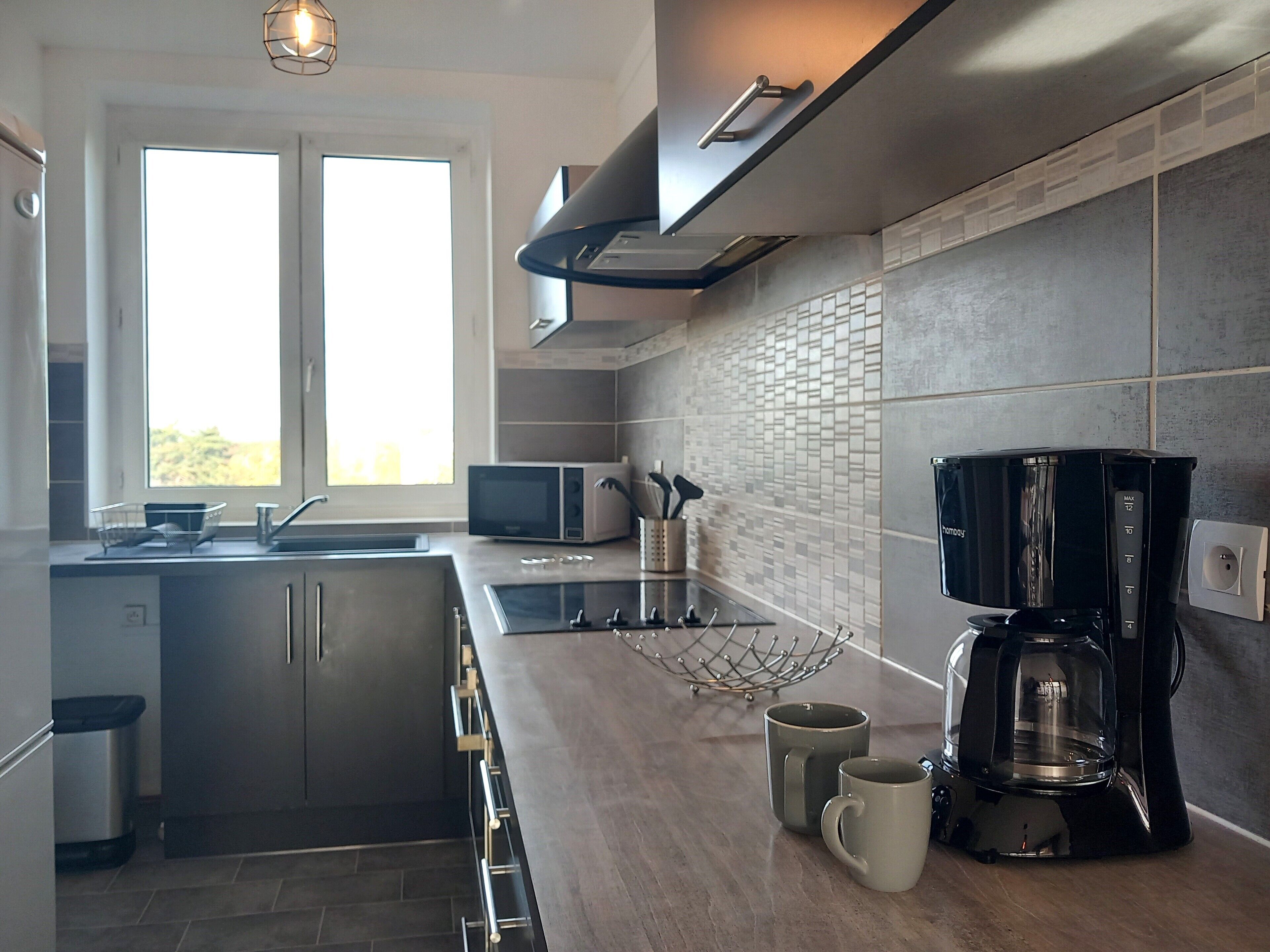 Een moderne keuken met een inbouwmagnetron, een koffiezetapparaat en een raam dat natuurlijk licht binnenlaat.