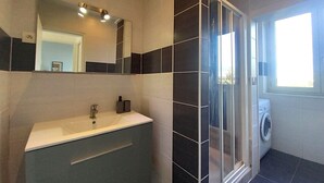 A modern bathroom with a white sink, a glass shower enclosure, and a window providing natural light. - Comfortable 3-bedroom T4 apartment (Mourenx)
