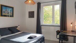 A bedroom with a bed, a desk, a chair, a hanging light fixture, a framed picture, and a departure board. - Comfortable 3-bedroom T4 apartment (Mourenx)