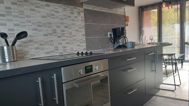 A modern kitchen with a built-in oven, stainless steel appliances, and a tiled backsplash. - Comfortable 3-bedroom T4 apartment (Mourenx)