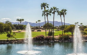 A golf course with two water fountains, palm trees, and mountains in the background. - Well maintained and perfectly appointed 3 bedroom/2 bath home in The Grand (Surprise)