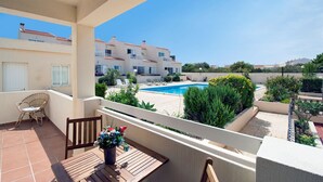 En balkon med udsigt til en swimmingpool, et træbord og en fletstol.