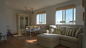 En stue med sofa, spisebord med stole, skab og store vinduer.