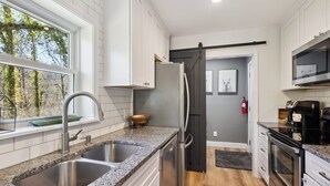 Una cocina moderna con encimeras de granito, electrodomésticos de acero inoxidable y un amplio ventanal con vistas a un bosque.