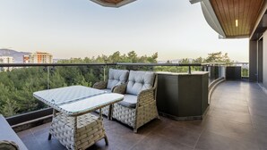 Un balcon agrémenté de meubles en osier, d’une table en verre et offrant une vue sur la verdure et les bâtiments.