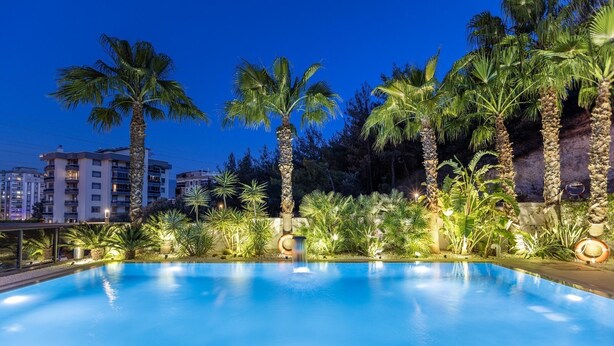 Une piscine entourée de palmiers et de verdure, avec des bâtiments en arrière-plan.