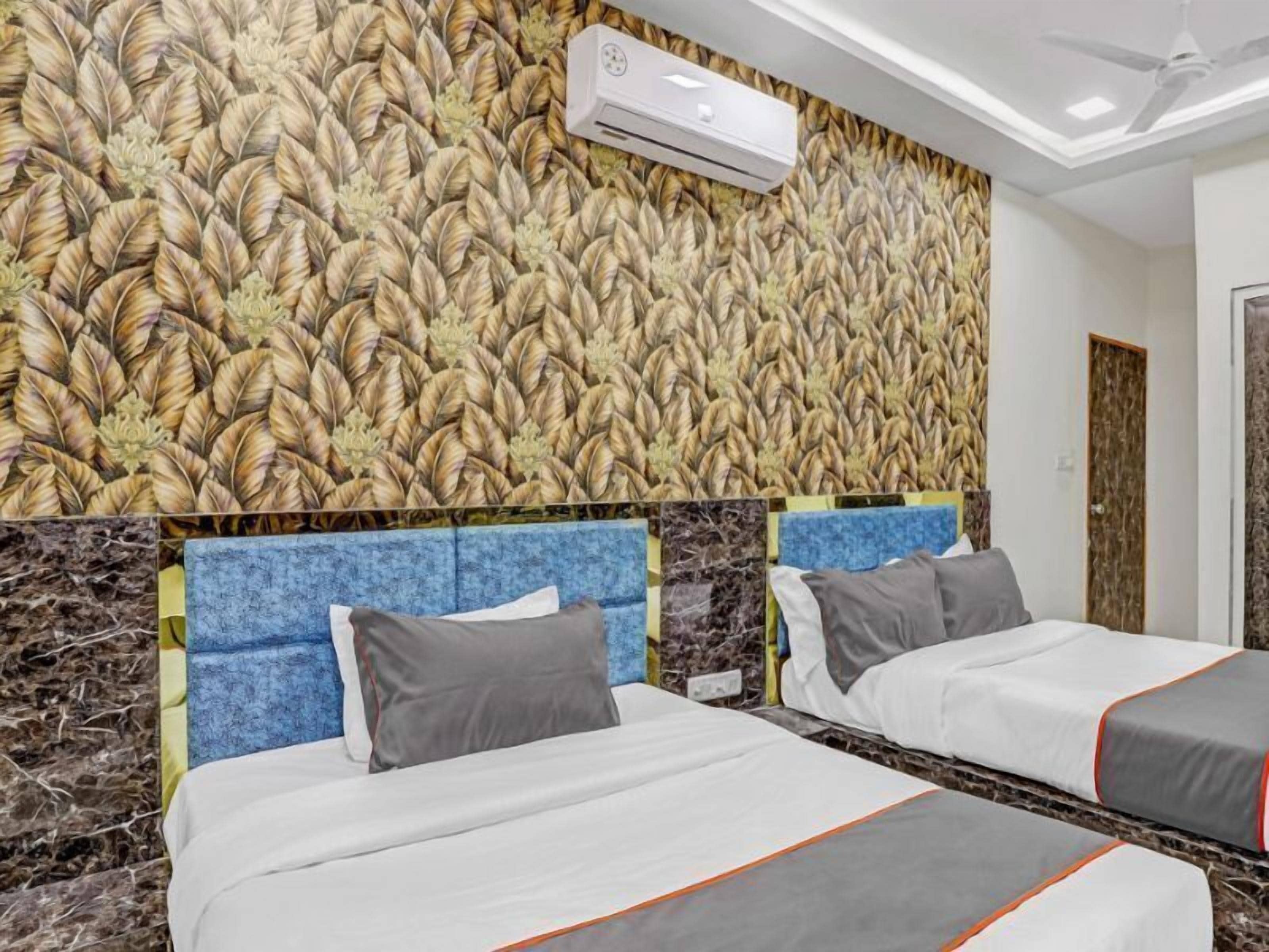 A hotel room with two beds, a patterned wall, an air conditioning unit, and a ceiling fan.