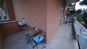 Ein Balkon mit Holztisch und -stühlen, einem kleinen Waschbecken und einem Geländer.