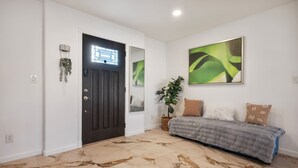 A room with a dark door, a light-colored wall, a grey sofa, and a large abstract painting.