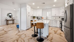 A modern kitchen with white cabinets, a central island with bar stools, a stainless steel refrigerator, and a marble floor.