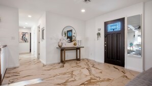 A hallway with a marble floor, a dark door, and a mirror above a console table.