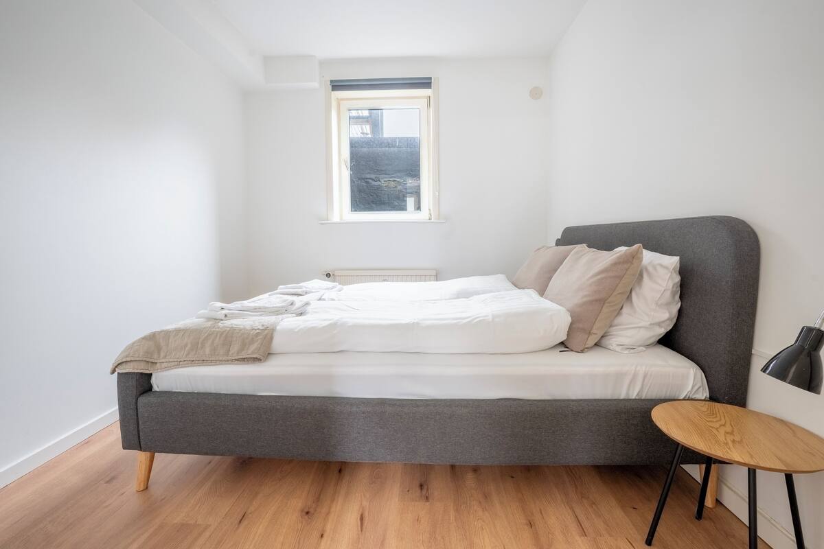 A bedroom with a bed, a small round table, and a window.