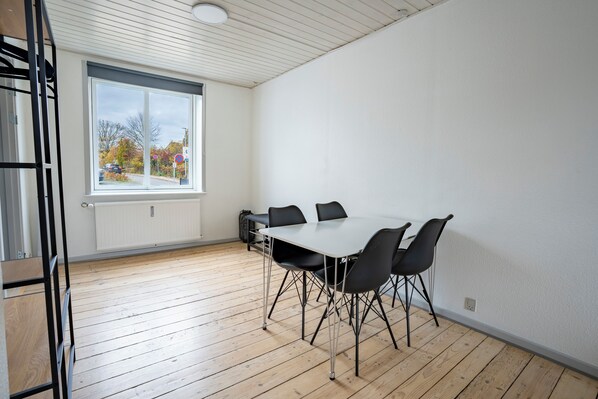 Una habitación con un ventanal grande, una mesa blanca con sillas y suelo de madera.