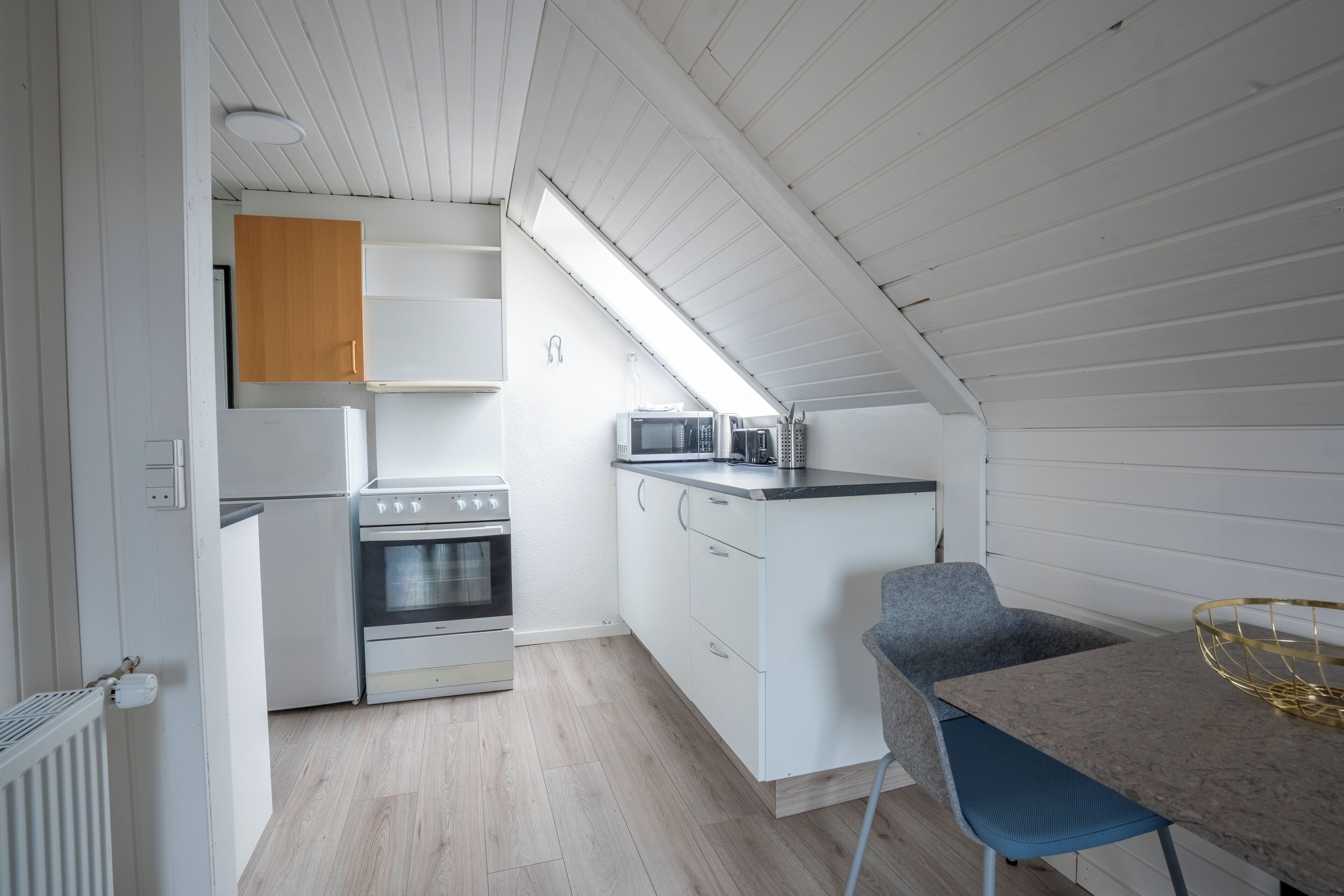A compact kitchen with white cabinetry, a built-in oven, a microwave, and a small dining area with a table and chair.