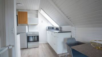 Una cocina compacta con armarios blancos, horno empotrado, microondas y un pequeño comedor con mesa y silla.