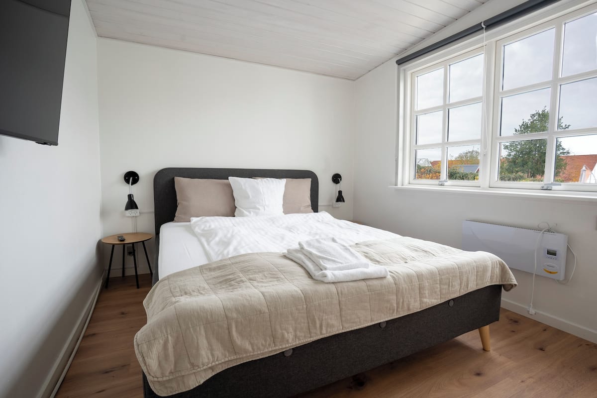 A bedroom with a bed, bedside tables, a window, and a wall-mounted heater.