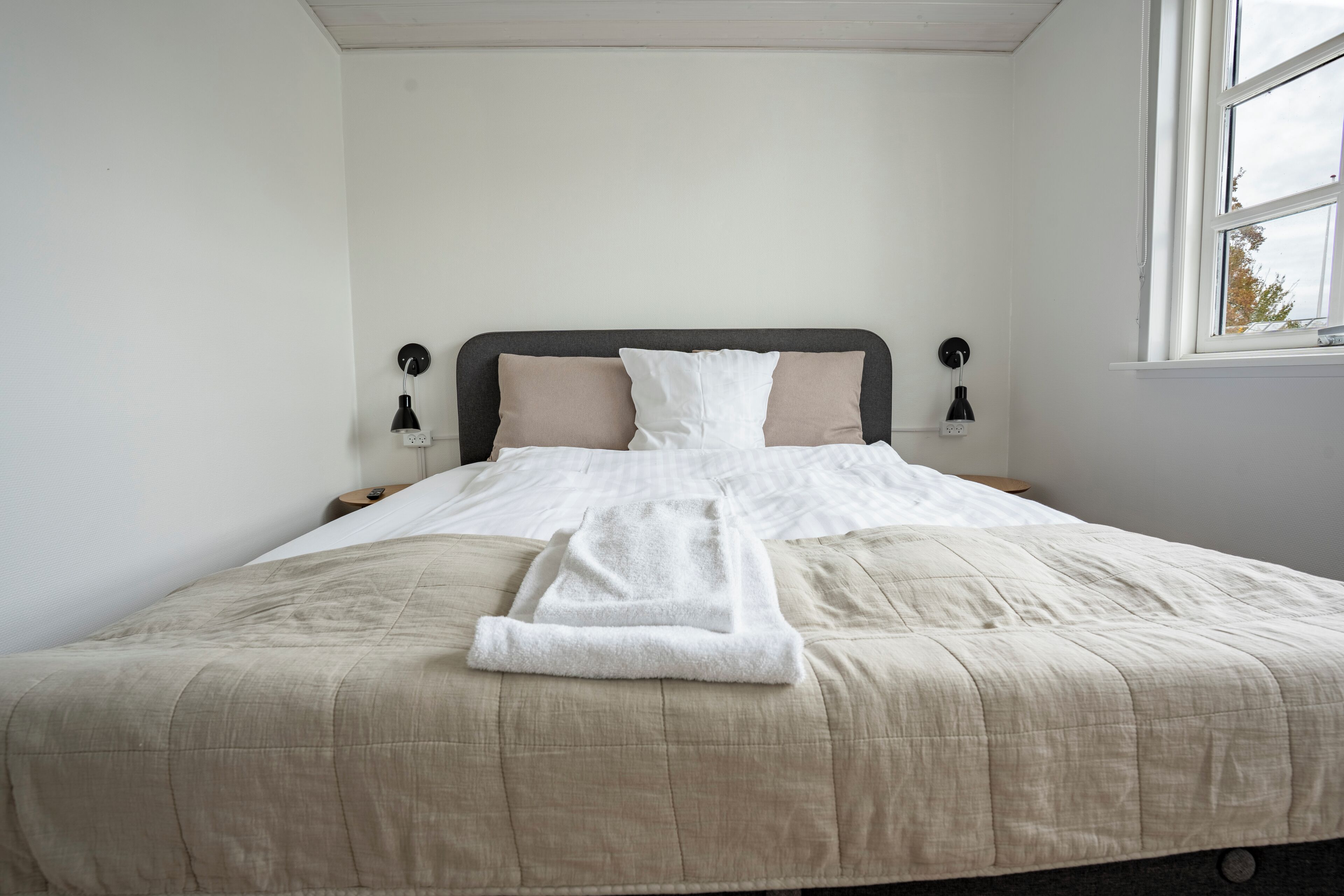 A neatly made bed with a beige comforter and pillows, a white towel, and two bedside lamps.